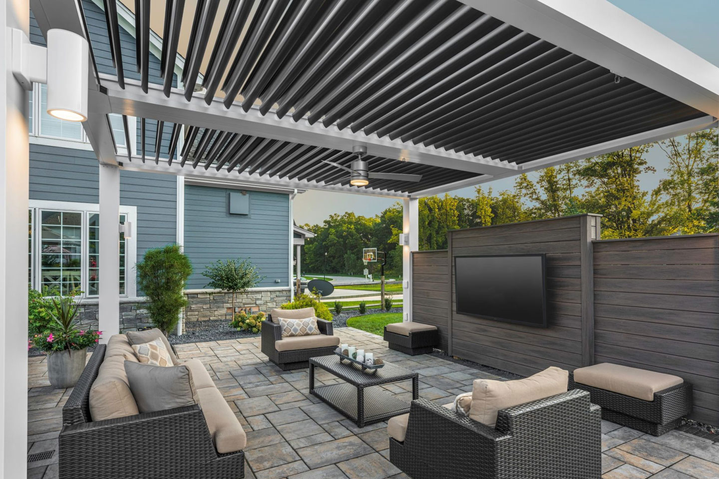 Luxury outdoor living room under a motorized louvered roof system, showcasing a custom patio design with wicker furniture, ambient lighting, and high-end weather protection installed by Decadent Outdoors.