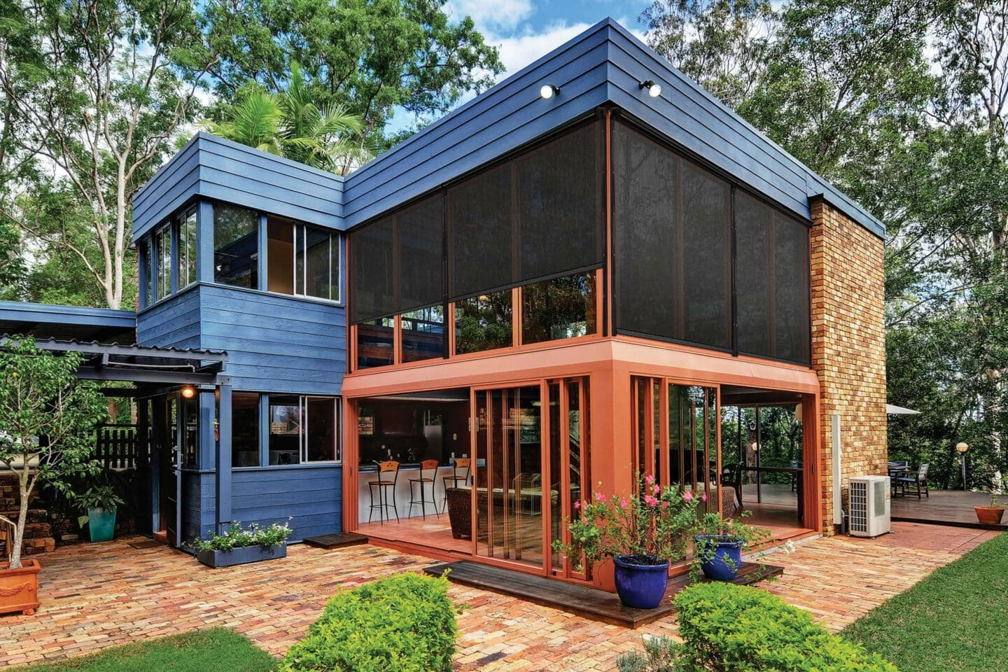 Modern two-story home featuring SummerSpace motorized power screens by Decadent Outdoors, providing solar protection and insect control for a large second-floor balcony and open-concept lower patio area.