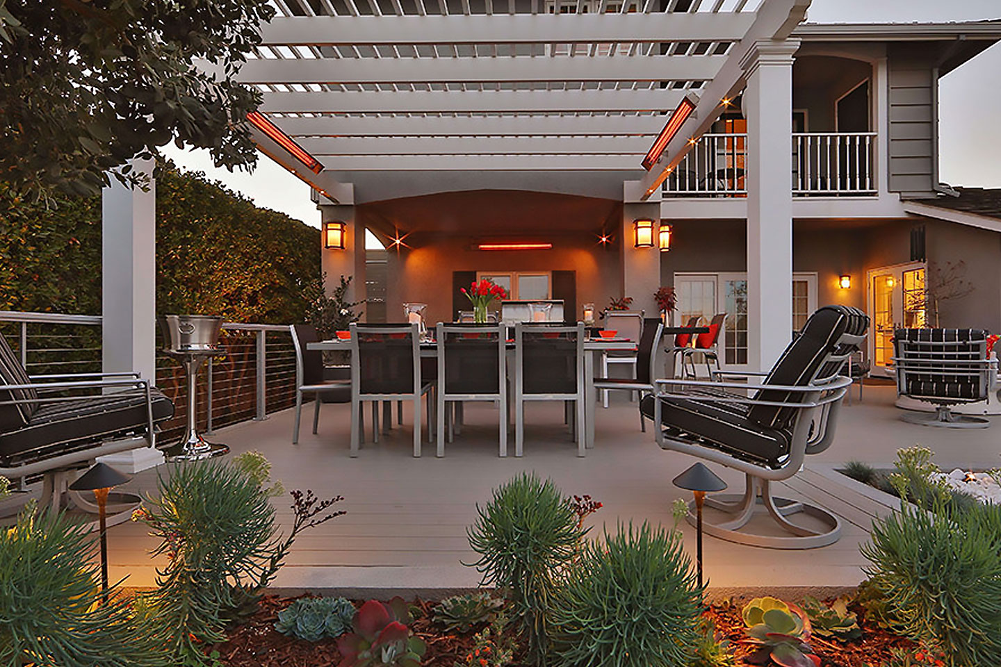 Luxury outdoor dining deck by Decadent Outdoors featuring a white pergola with integrated Infratech infrared heaters, ambient pathway lighting, and a modern dining set for year-round comfort.