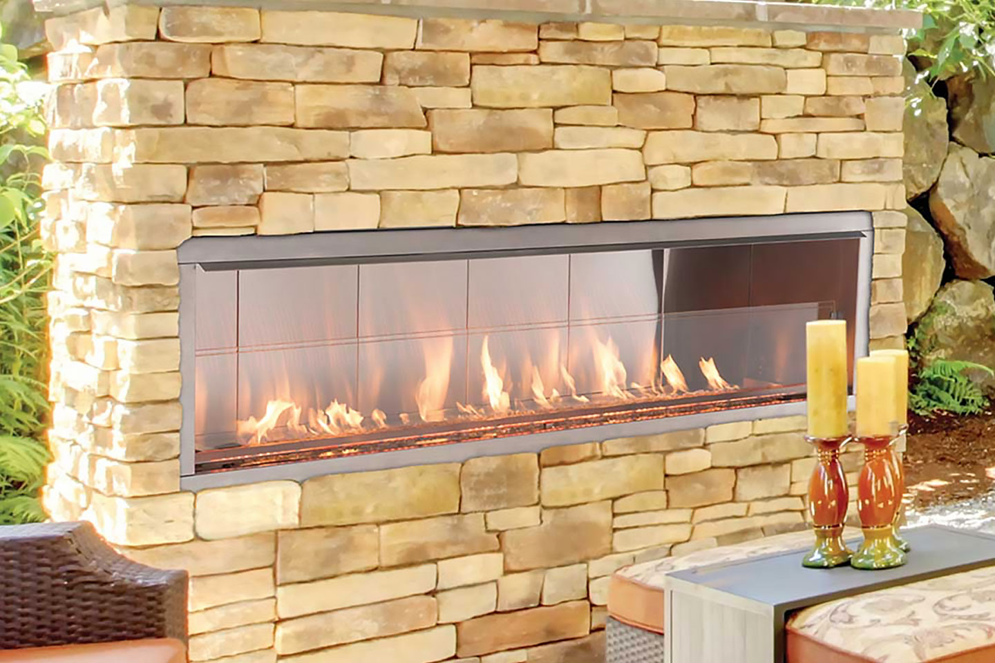 Modern outdoor linear gas fireplace with a stacked stone masonry surround and glass burner, custom-designed by Decadent Outdoors for a luxury backyard patio entertainment area.