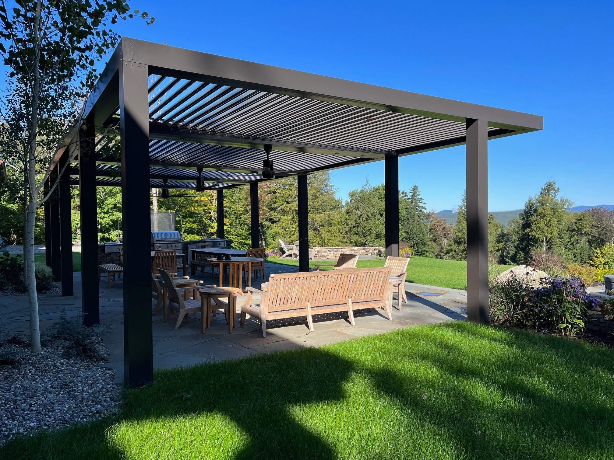 A large pergola with seating, and a view of the trees and distant mountains.