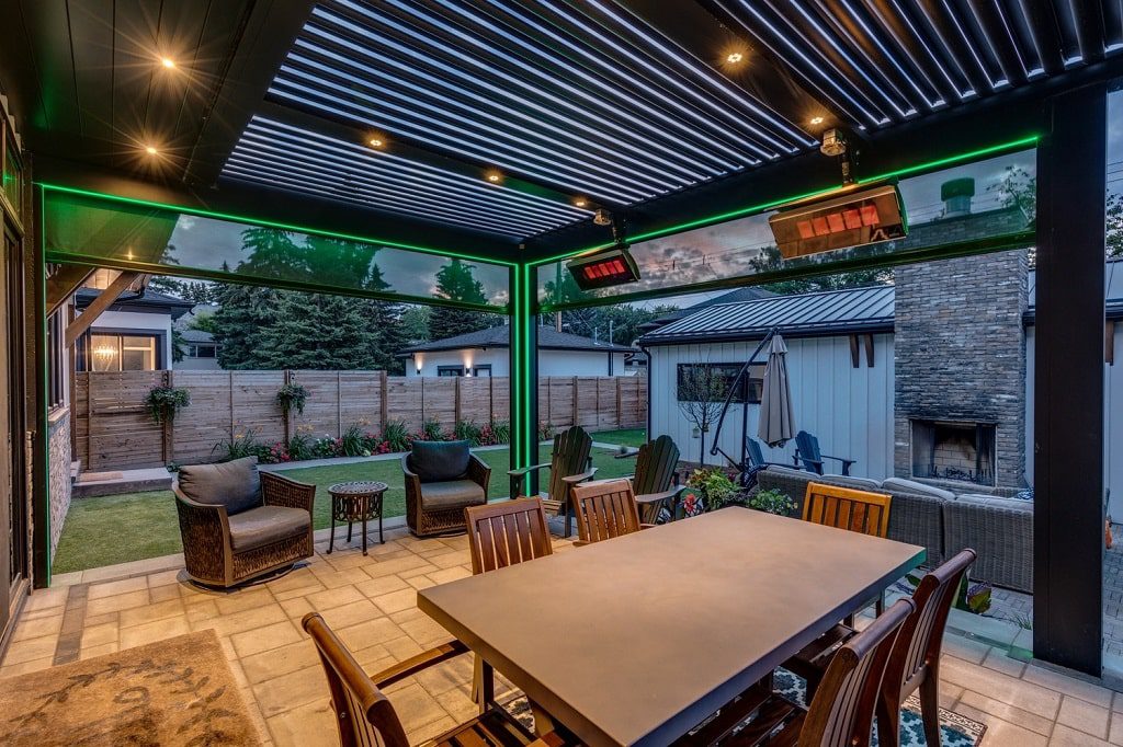 A StruXure pergola that has recessed white lighting on the ceiling, as well as more dramatic green lighting around the structure openings.
